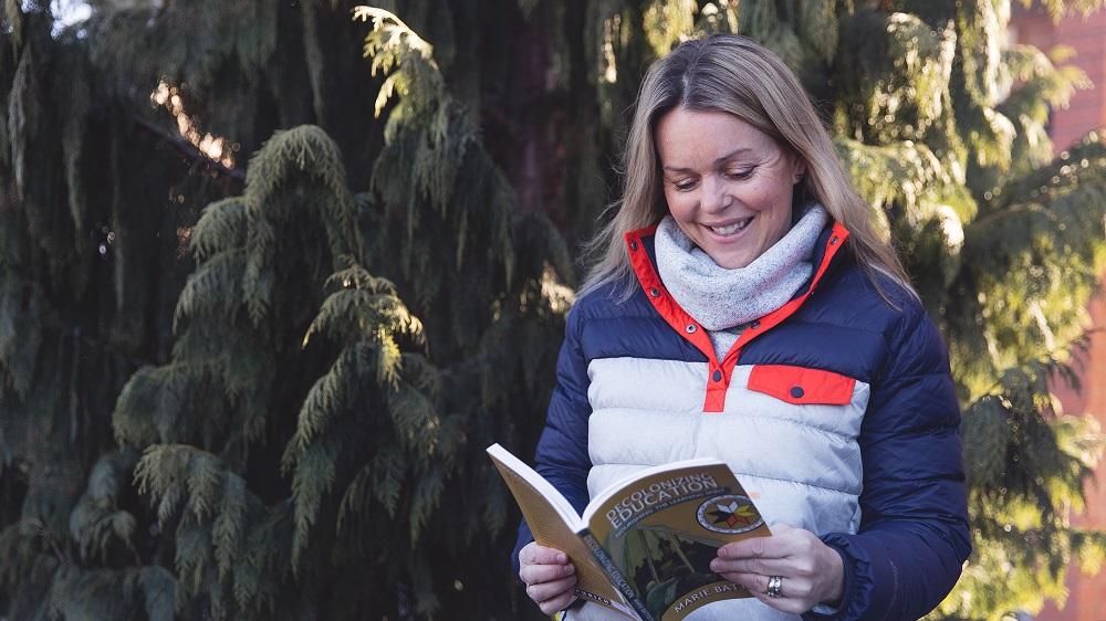 Courtney Morgan standing in front of tree holding book