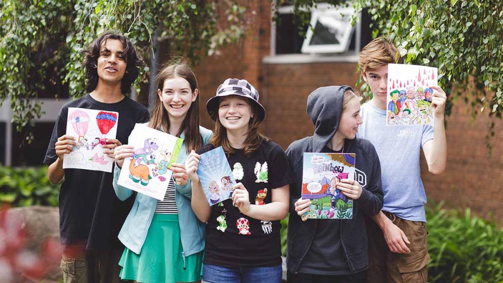 Students standing outside of school holding up school project