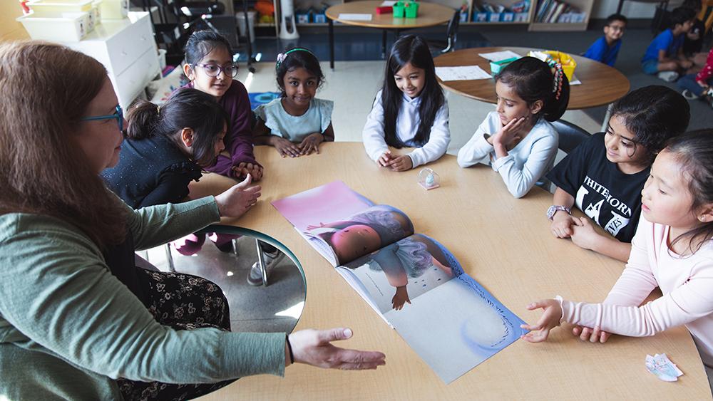 Heather Thompson sitting with students at round table reading a book