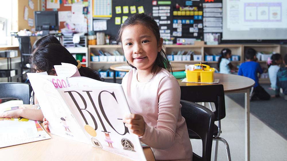 Girl in classroom reading the book titled "Big"