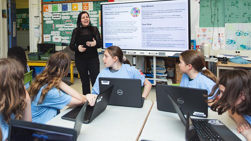 Teacher standing in front of a classroom of girls using laptops
