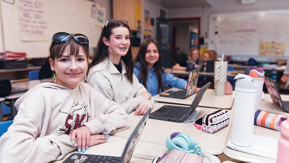 Students sitting around desk that has laptops on it
