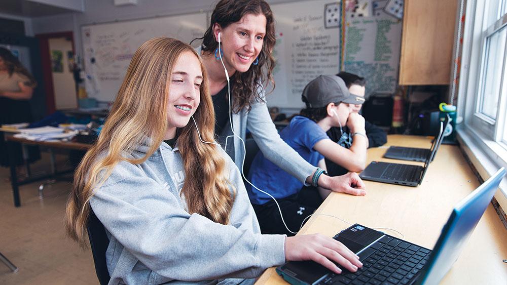 Two students sharing earbuds while looking at laptop