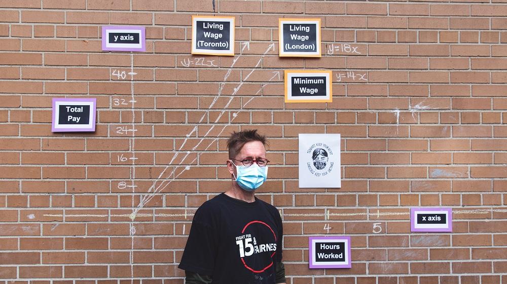 David Stocker standing in front of student project on wall outside of school