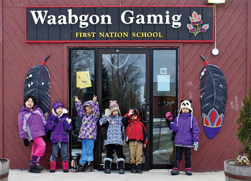 Young children in winter wear standing out front of Waabgon Gamig First Nation School