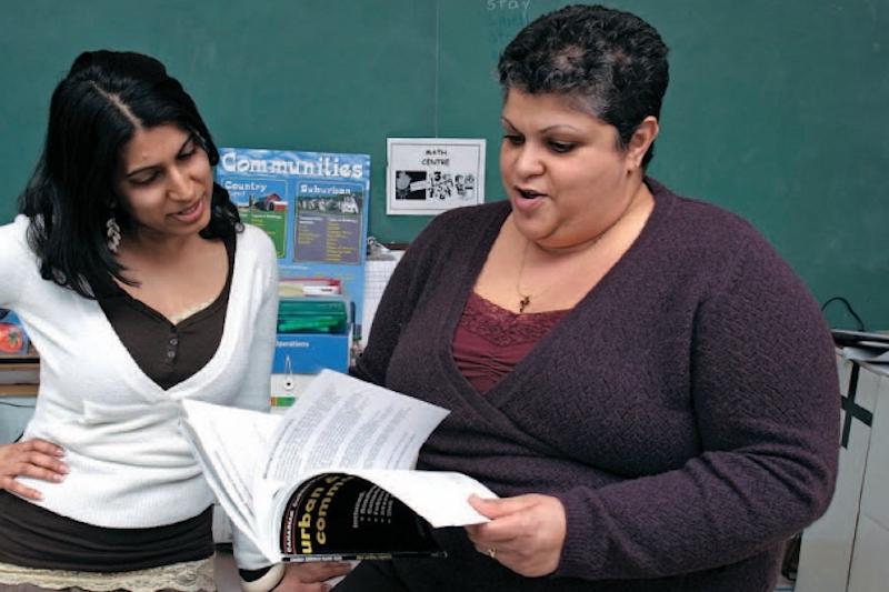 Two teachers flipping through textbook