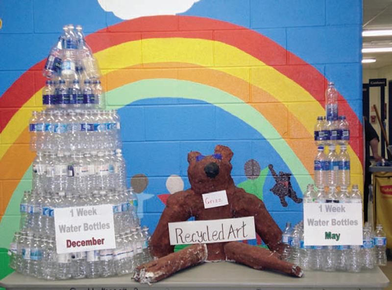 student project of towers constructed from water bottles with a rainbow painted on brick wall in background