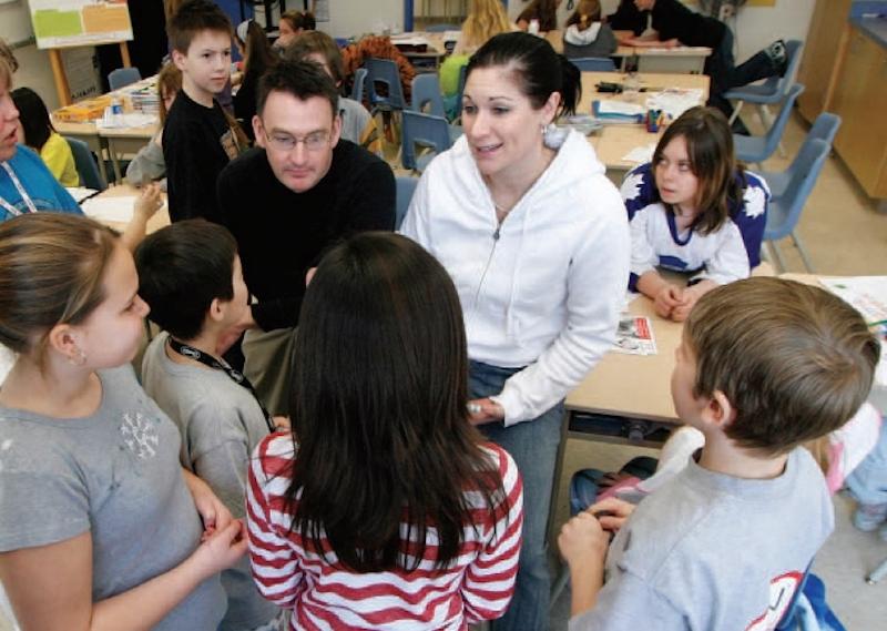 Teacher standing with students providing an explenation