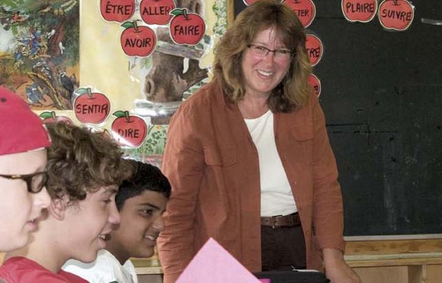 Teacher smiling at front of classroom with three students in foreground