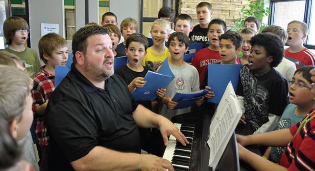 music teacher singing and playing keyboard surrounded by students who are also singing