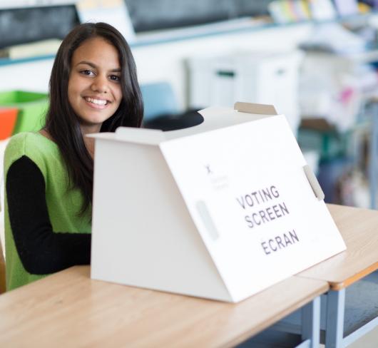 Student volunteer sitting next to vote submission box