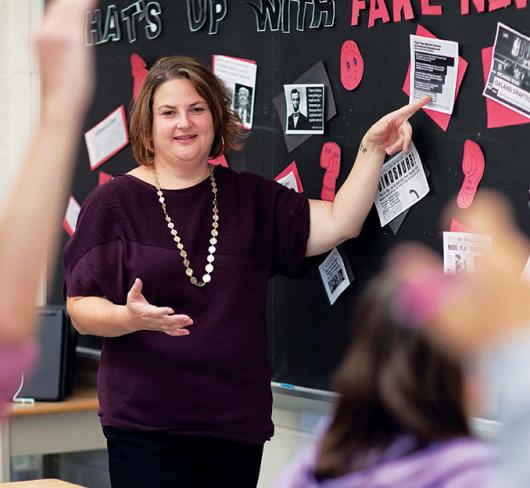 teacher in front of classroom pointing at fake news