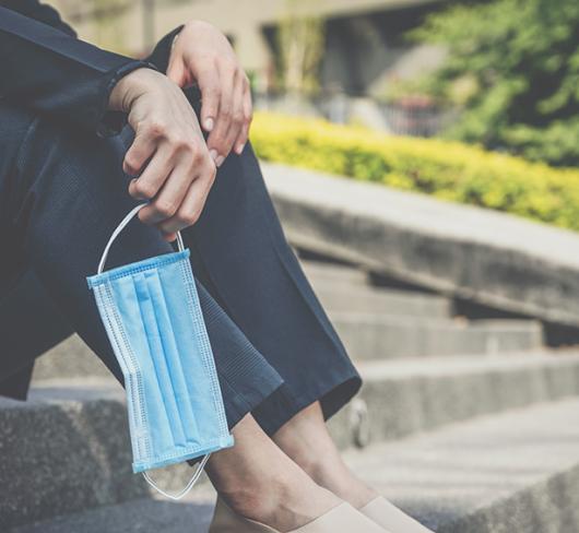 Woman sitting on steps holding medical mask