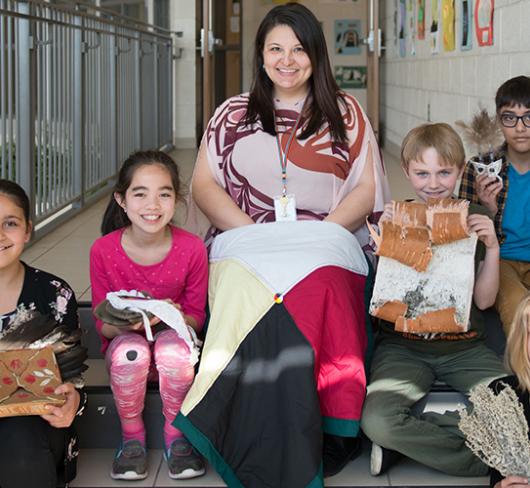 teacher and students sitting on stairs displaying indigenous history projects