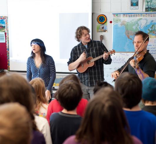 three musicians performing in front of classroom of elementary students