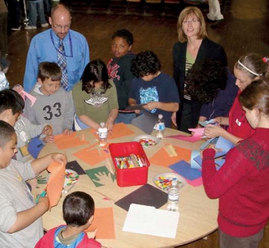 students standing at round table creating art from construction paper