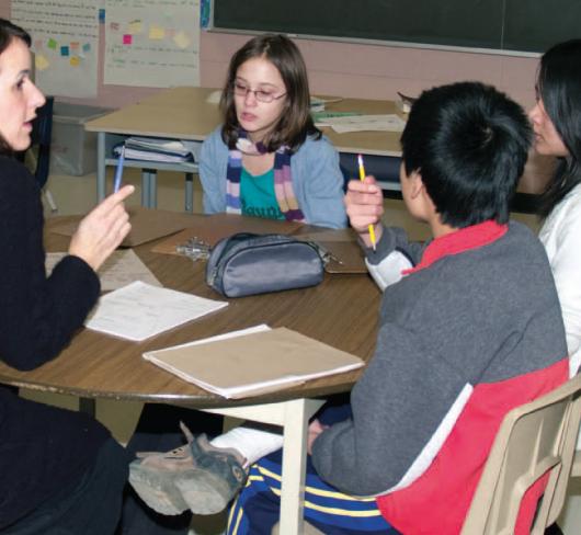 teacher sitting with three elementary students at a desk in classroom