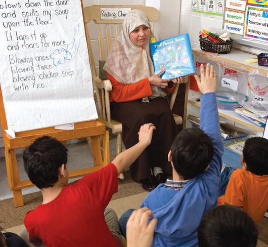 Teacher reading book to students with their hands up