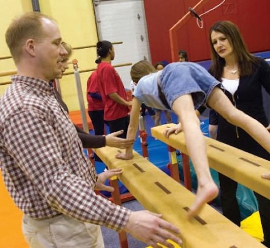 Two teachers teaching young student how to use gymnasium equipment