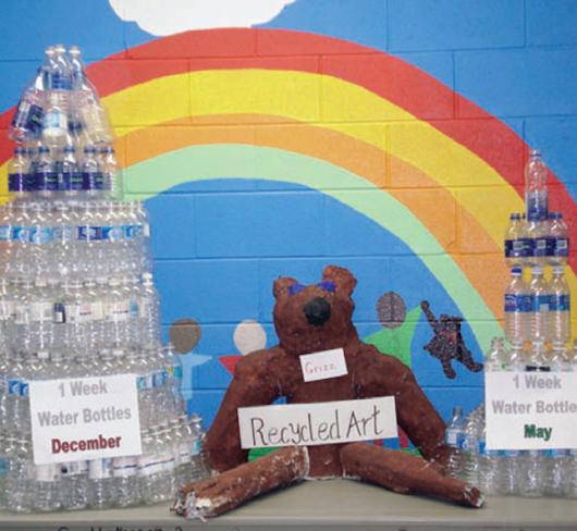 student project of towers constructed from water bottles with a rainbow painted on brick wall in background