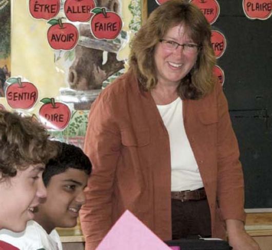 Teacher smiling at front of classroom with three students in foreground