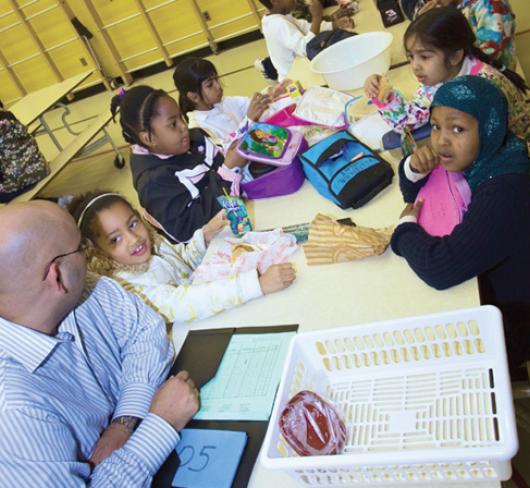 teacher sitting with students at large table in cafeteria