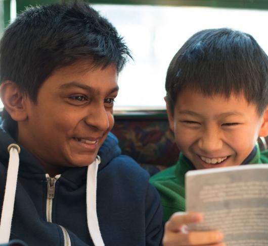Two elementary students laughing while reading a book