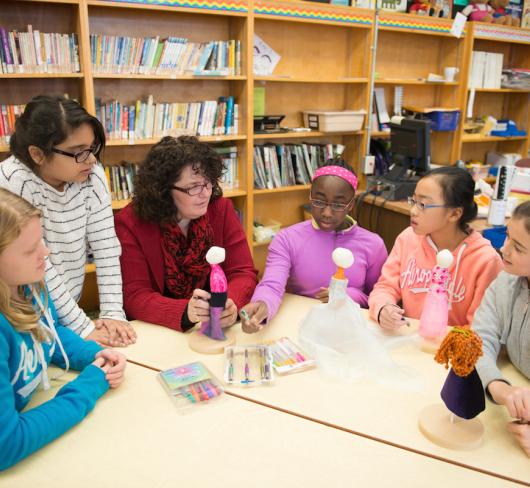 Elementary students and teacher sitting together working on dolls in library