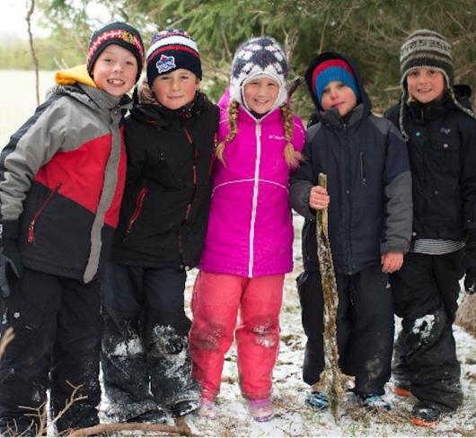 Children wearing snowsuits standing near wooded area