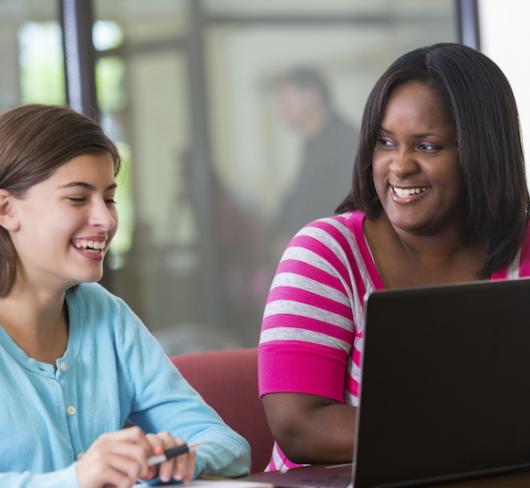 Teacher and student, smiling, looking at laptop 