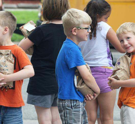 young elementary students standing together  near school bus holding paper bags