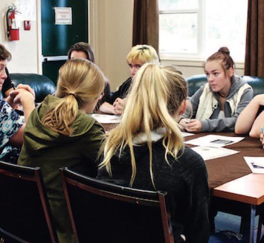 young teens, adults and a police officer sitting at boardroom table having discussion